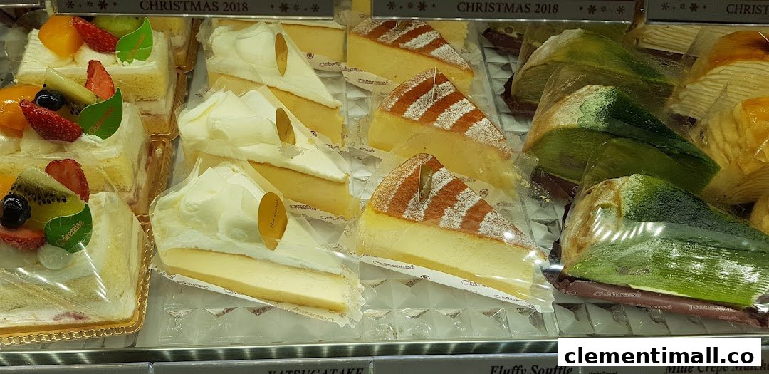 A vibrant display of various cakes, including fruit tarts, cheesecakes, and matcha crepes, in a retail display.