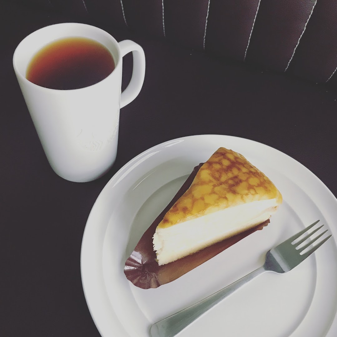 A delicious slice of cake and a warm cup of tea on a white plate, ready to be enjoyed.
