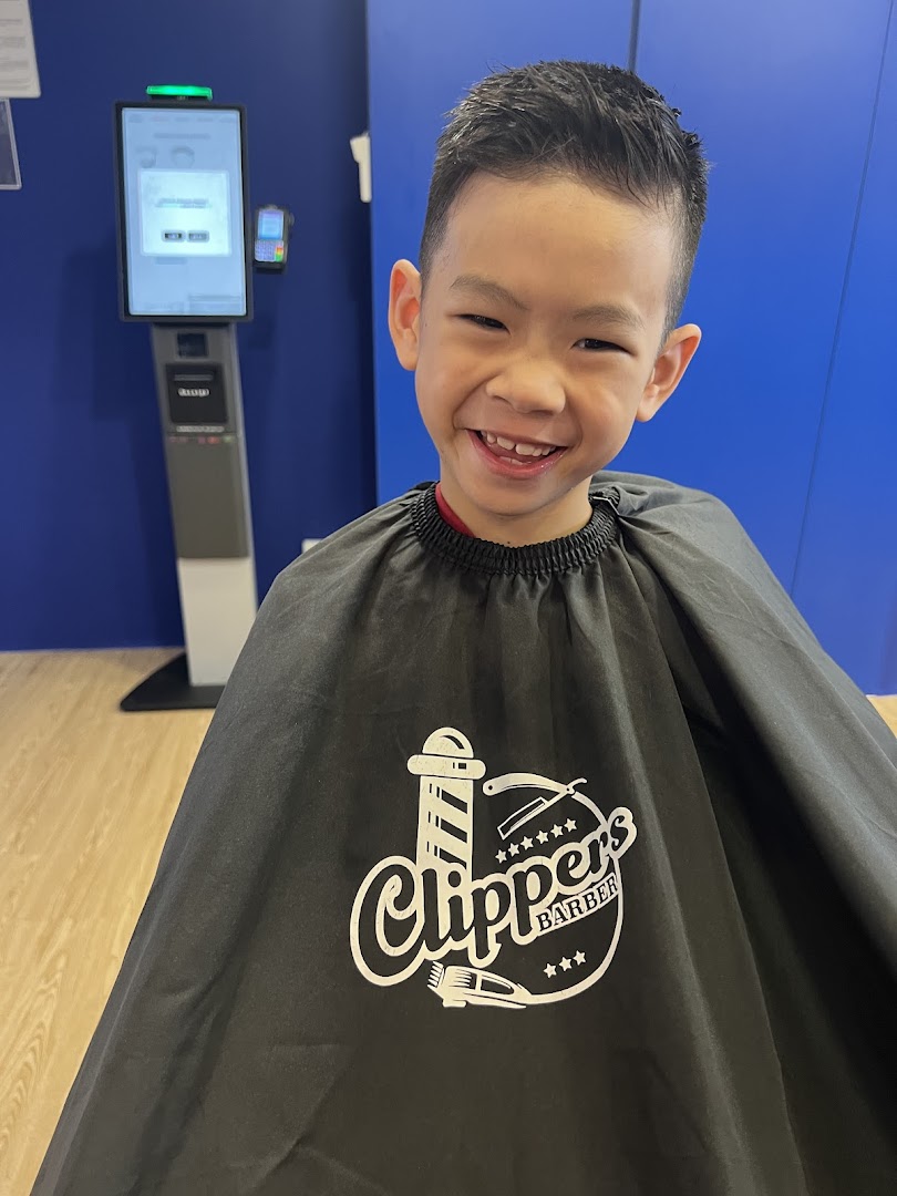 A happy child in a barber's cape with the Clippers Barber logo, showing a fresh haircut.