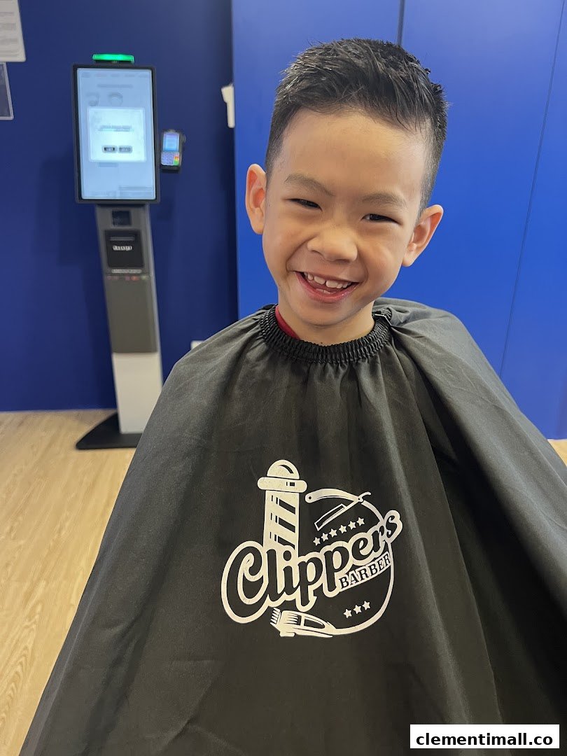 A happy child in a barber's cape with the Clippers Barber logo, showing a fresh haircut.