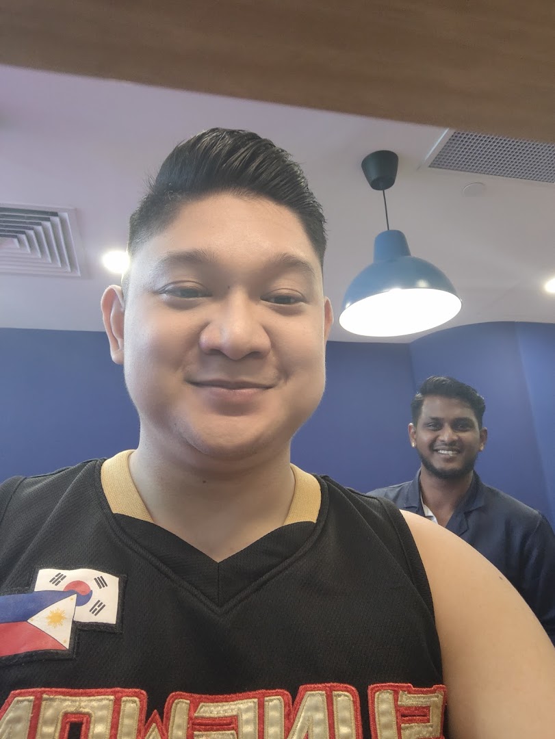Two smiling men inside Clippers Barber, one in the foreground with a fresh haircut.