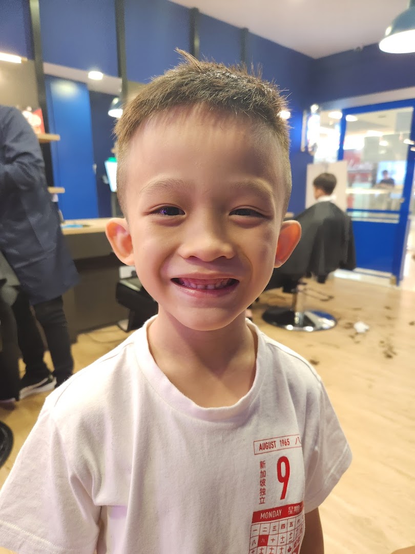 A happy child smiles after a fresh haircut inside Clippers Barber, showcasing a family-friendly atmosphere.