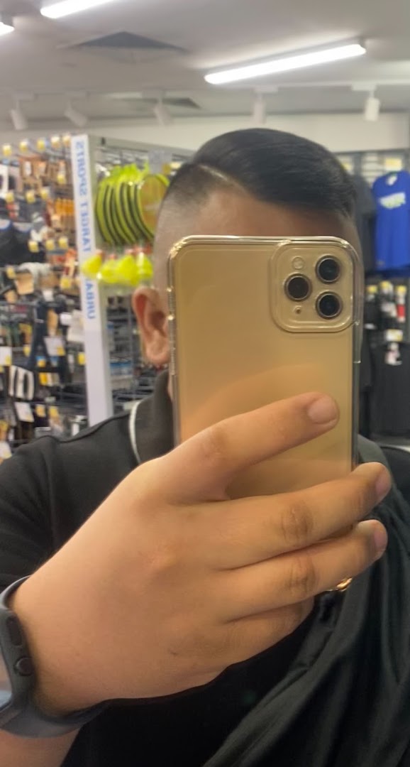 A person takes a selfie, showcasing a fresh haircut with a retail store background.
