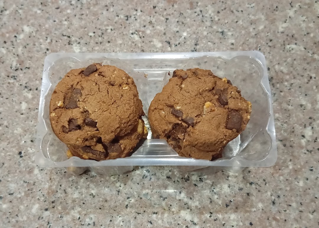 Two chocolate chip cookies in a clear plastic container on a speckled countertop.
