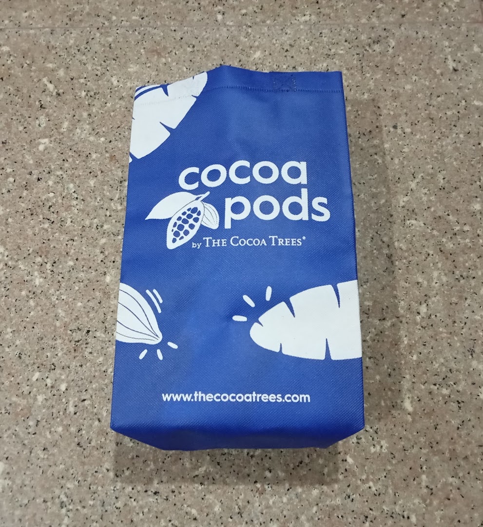 A blue shopping bag featuring the 'Cocoa Pods by The Cocoa Trees' logo and website.