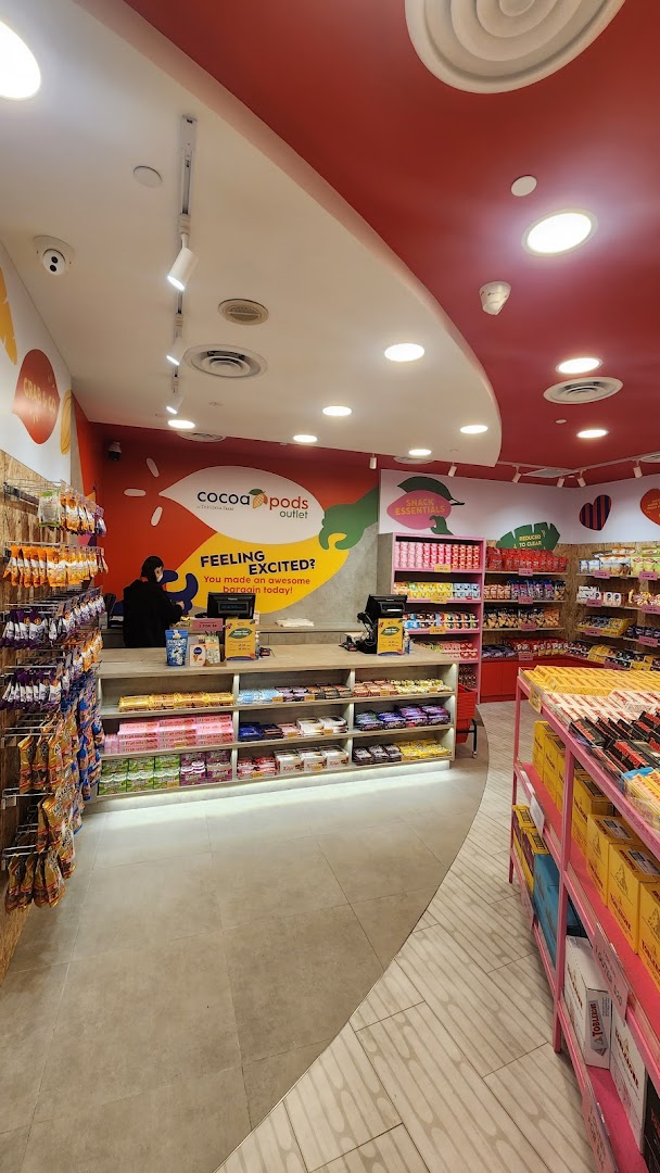 An interior view of Cocoa Pods outlet, featuring shelves of snacks, chocolates, and a cashier at the counter.