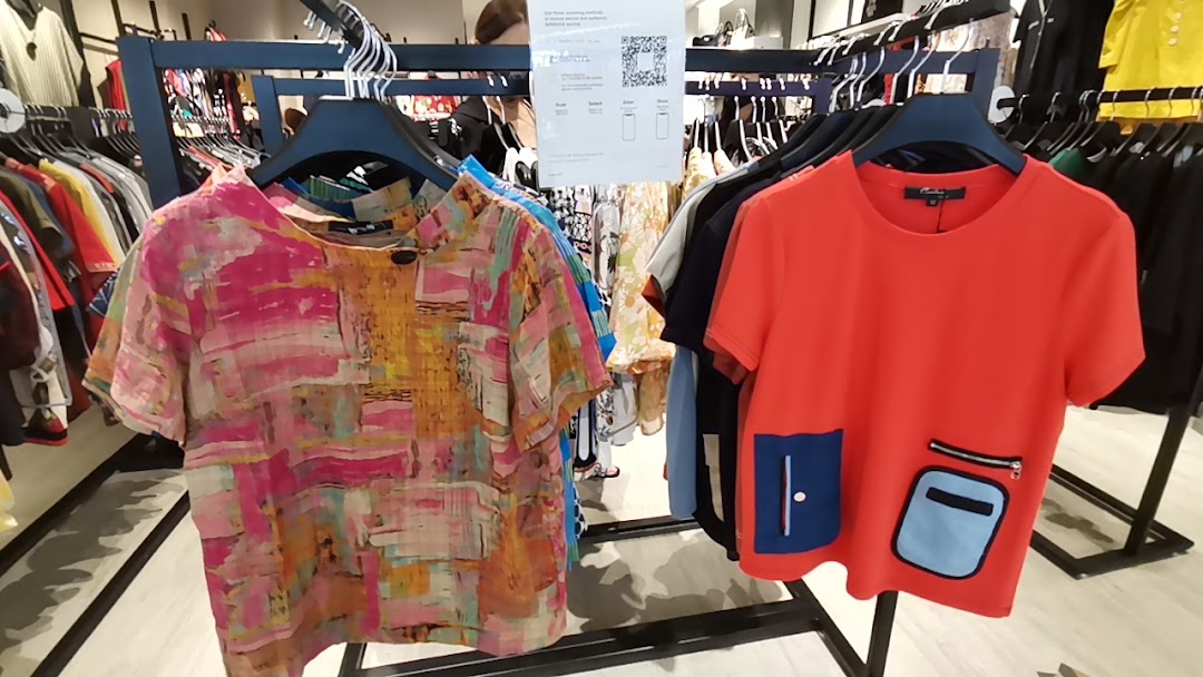 Two stylish tops, one colorful abstract and one red with unique pockets, displayed on a clothing rack.