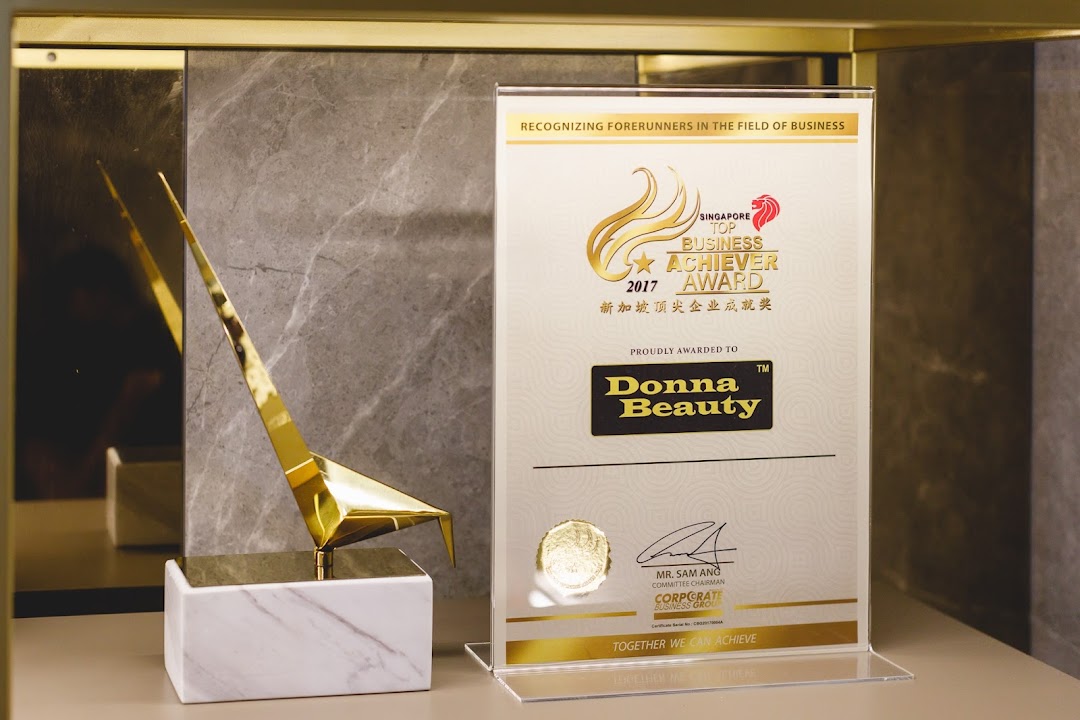 A golden trophy displayed next to the 'Singapore Top Business Achiever 2017' award for Donna Beauty.