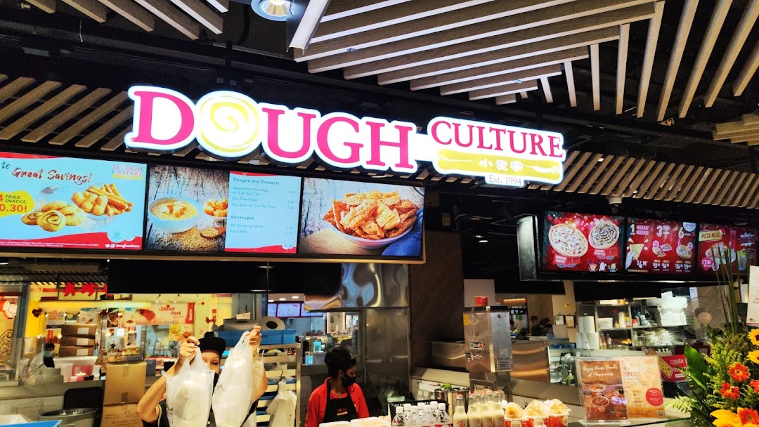 A bustling counter at Dough Culture with staff serving customers and digital menu displays.