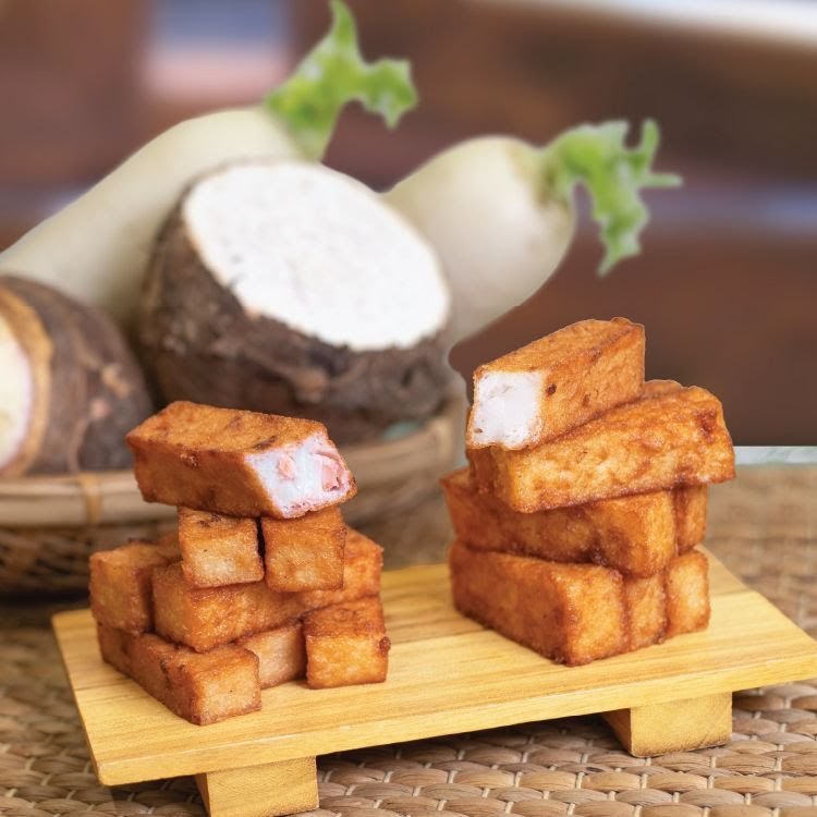 Close-up of fried radish and taro cakes with fresh radish and taro in the background.