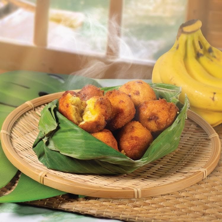 Steaming hot golden-fried banana fritters served in a banana leaf on a woven tray, with fresh bananas.