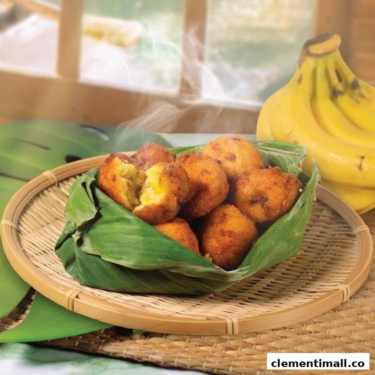 Steaming hot golden-fried banana fritters served in a banana leaf on a woven tray, with fresh bananas.