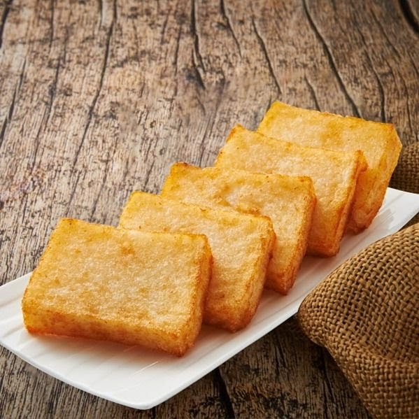 Golden fried radish cakes arranged on a white plate against a rustic wooden background.