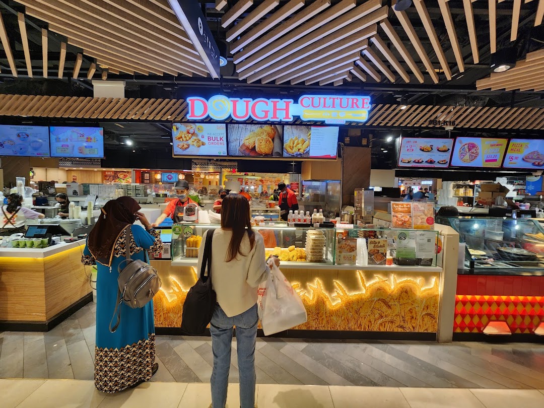 Customers at Dough Culture's counter, showcasing various baked goods and digital menu displays.
