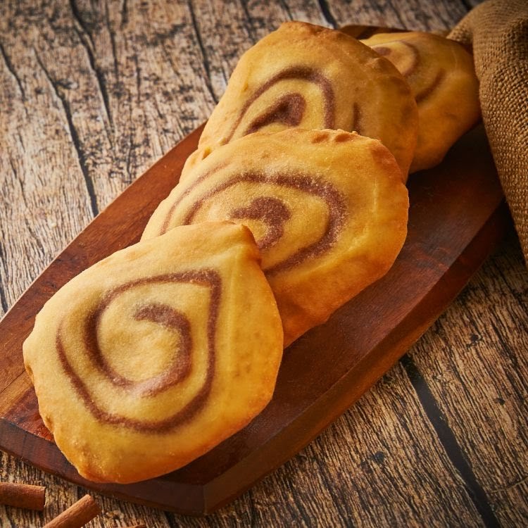 Golden-brown pastries with cinnamon swirls on a wooden board, with cinnamon sticks.