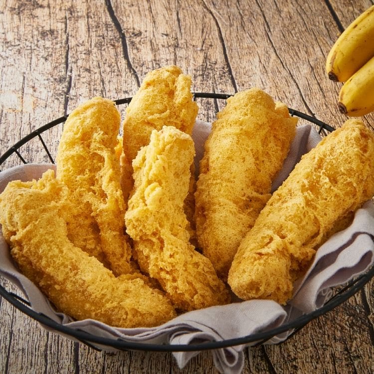 A basket of golden-brown fried bananas on a rustic wooden surface.