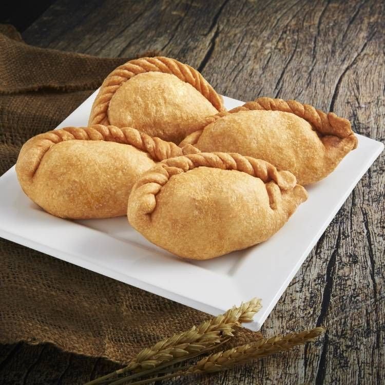 Four golden-brown, braided pastries, likely curry puffs or empanadas, presented on a white rectangular plate.