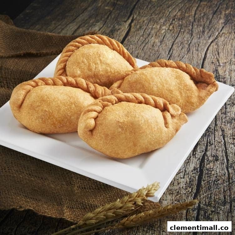 Four golden-brown, braided pastries, likely curry puffs or empanadas, presented on a white rectangular plate.