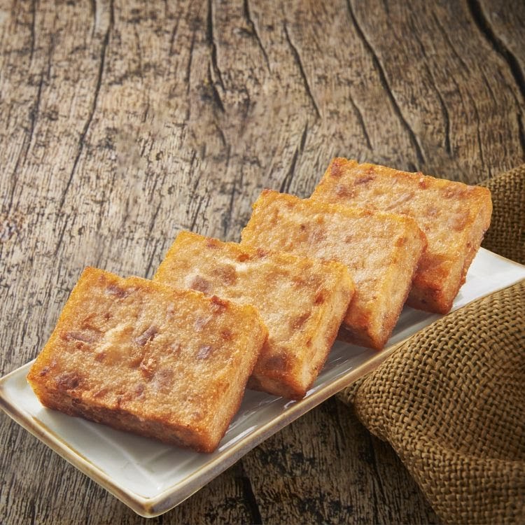 Four golden-brown fried savory cakes, possibly radish cake, on a white plate with a rustic wooden background.