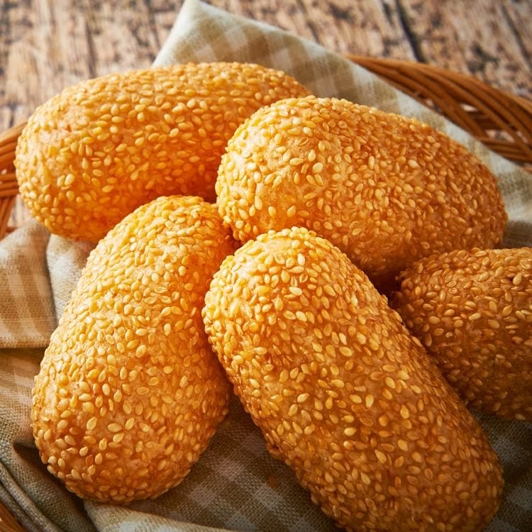 Close-up of golden-brown sesame-coated fried dough pastries in a basket.