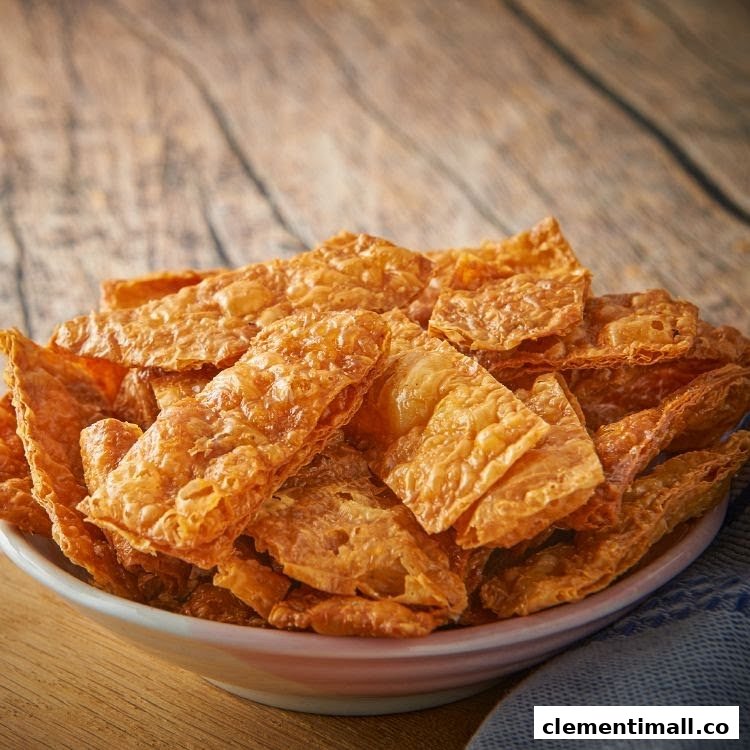 A bowl filled with golden-brown, crispy fried beancurd skin on a rustic wooden table.