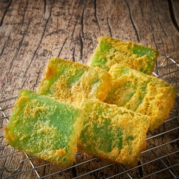 Vibrant green rectangular pastries, possibly kueh, dusted with yellow powder on a cooling rack.