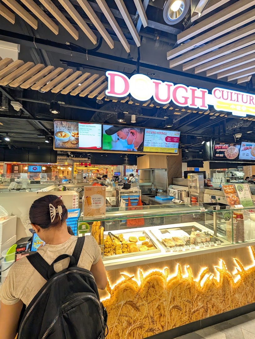 A customer at Dough Culture's counter, showcasing fresh pastries and digital menu screens.
