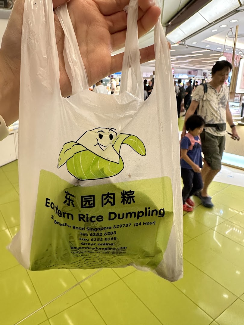 A person holds a plastic bag from Eastern Rice Dumpling, featuring its logo and contact details, inside a shopping mall.
