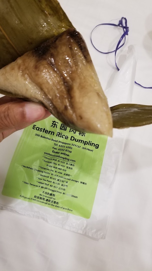 A hand holds a traditional rice dumpling with an 'Eastern Rice Dumpling' label showing shop details.