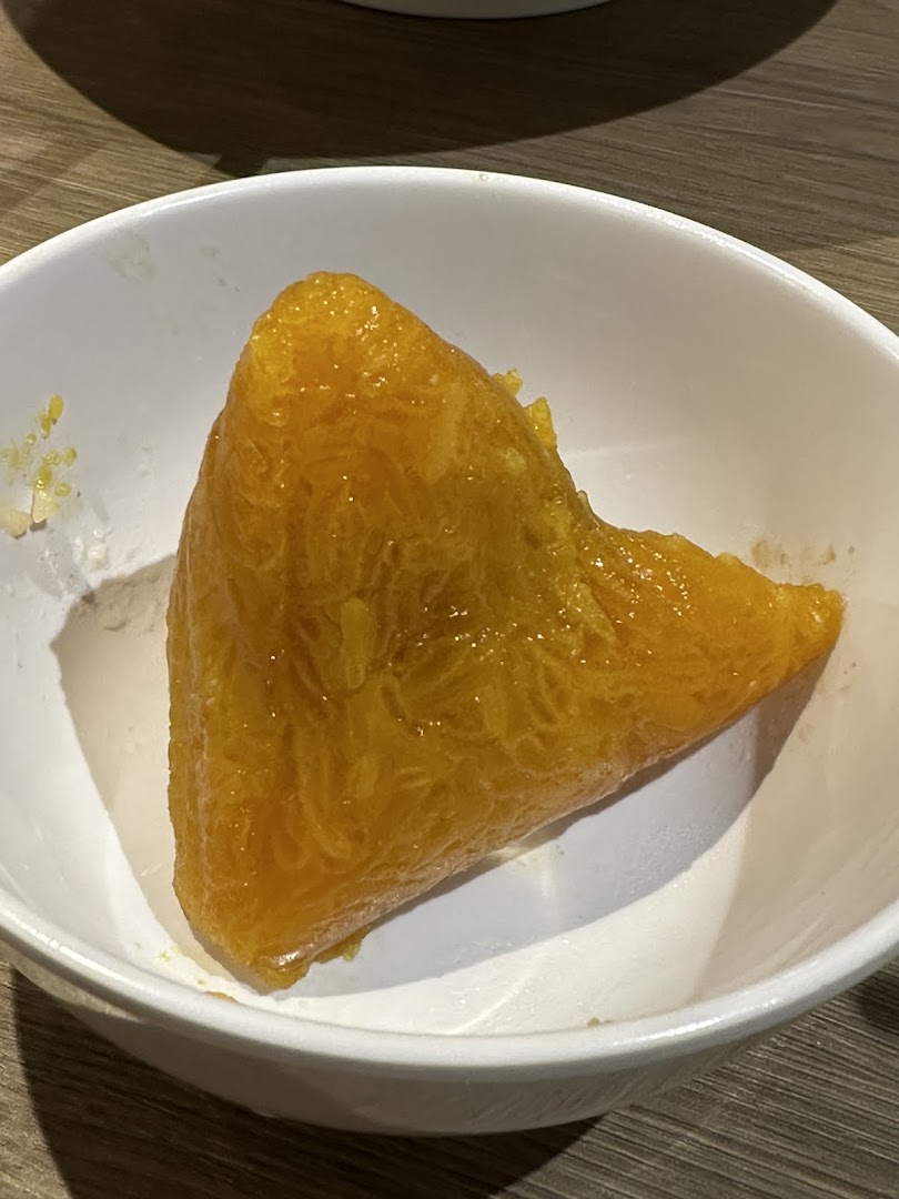 A vibrant golden-yellow rice dumpling, likely a sweet variety, served in a white bowl.