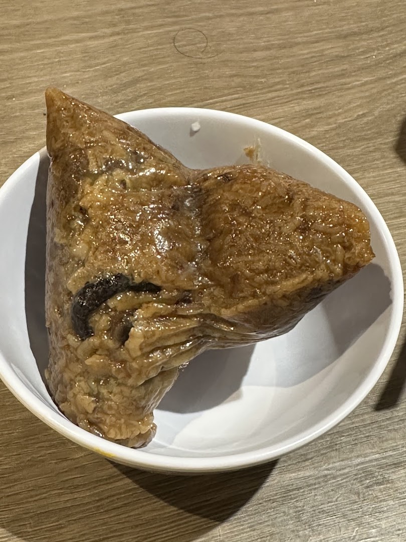 A traditional Chinese rice dumpling (zongzi) served in a white bowl on a wooden table.