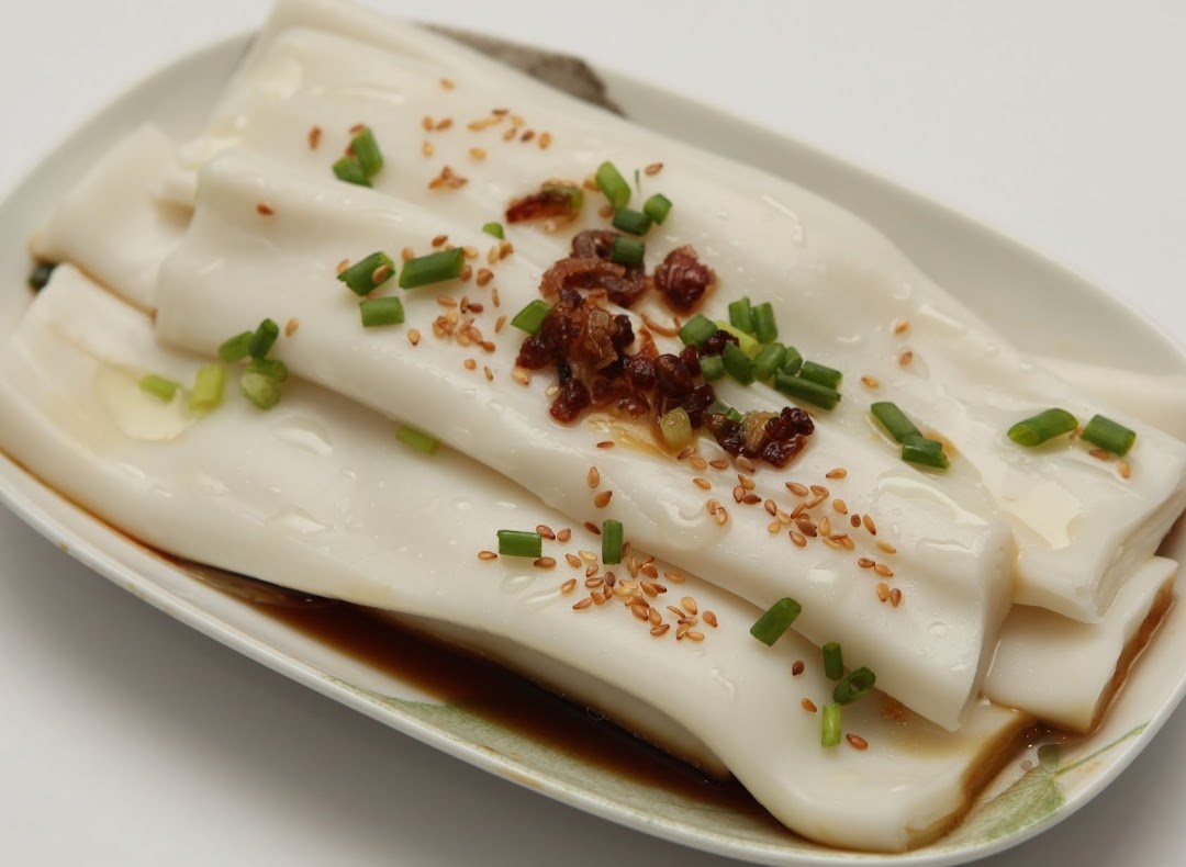 A close-up of delicious rice rolls (Cheung Fun) with sauce, sesame seeds, and green onions.