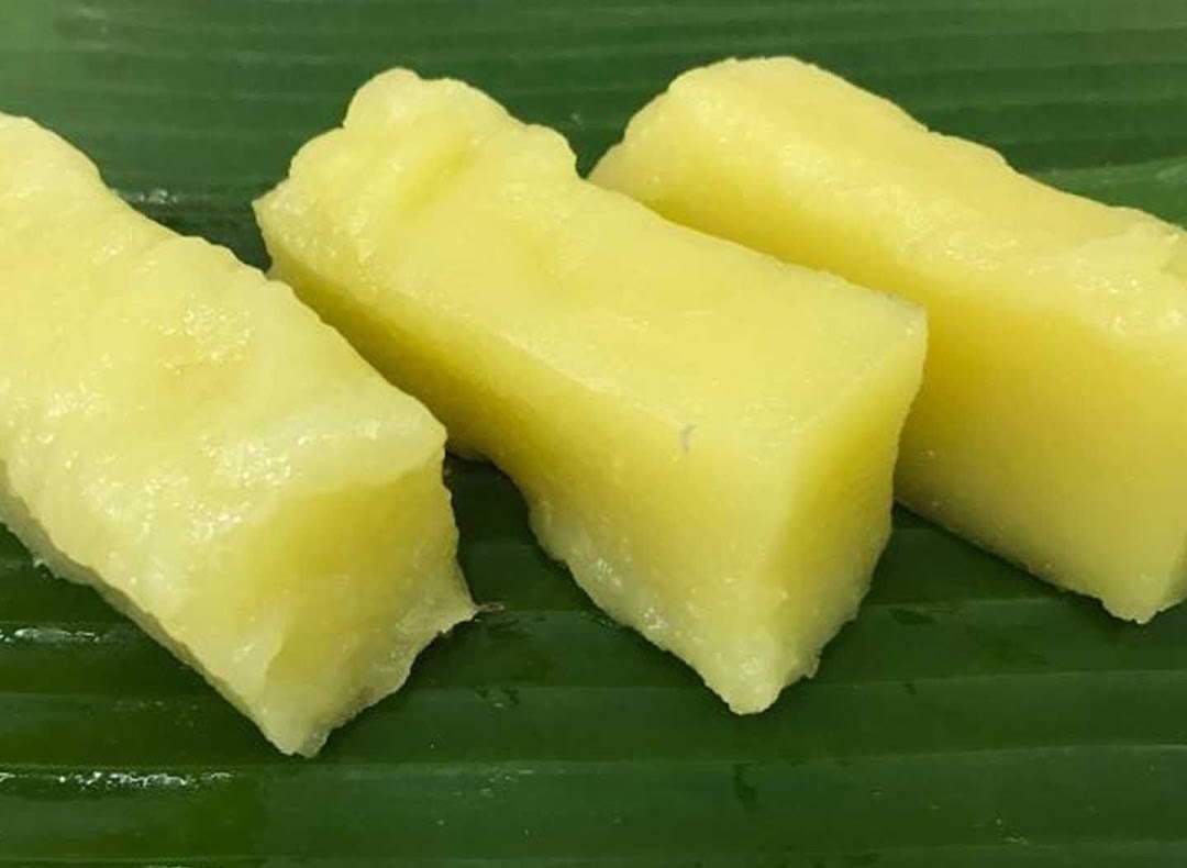 Three pieces of yellow, rectangular sweet treats or cakes on a green banana leaf.
