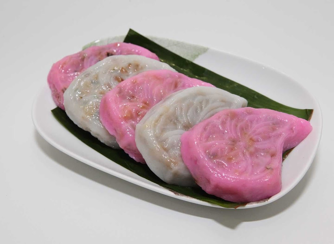 A plate of colorful, traditional dumplings, some pink and some white, on banana leaves.