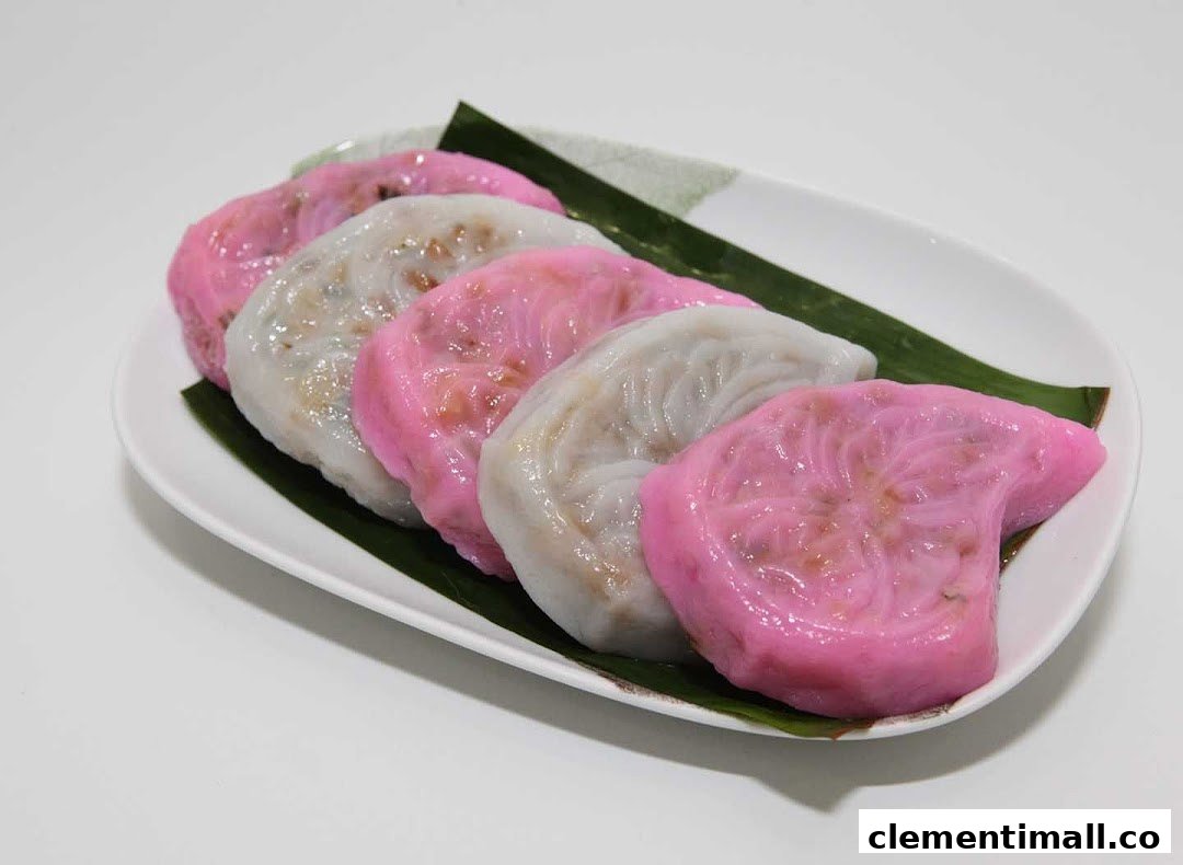 A plate of colorful, traditional dumplings, some pink and some white, on banana leaves.