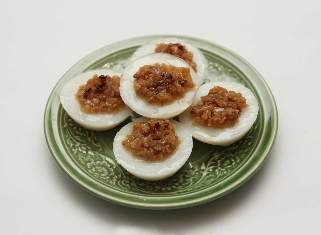 A green plate holds several white steamed rice cakes topped with savory brown minced ingredients.