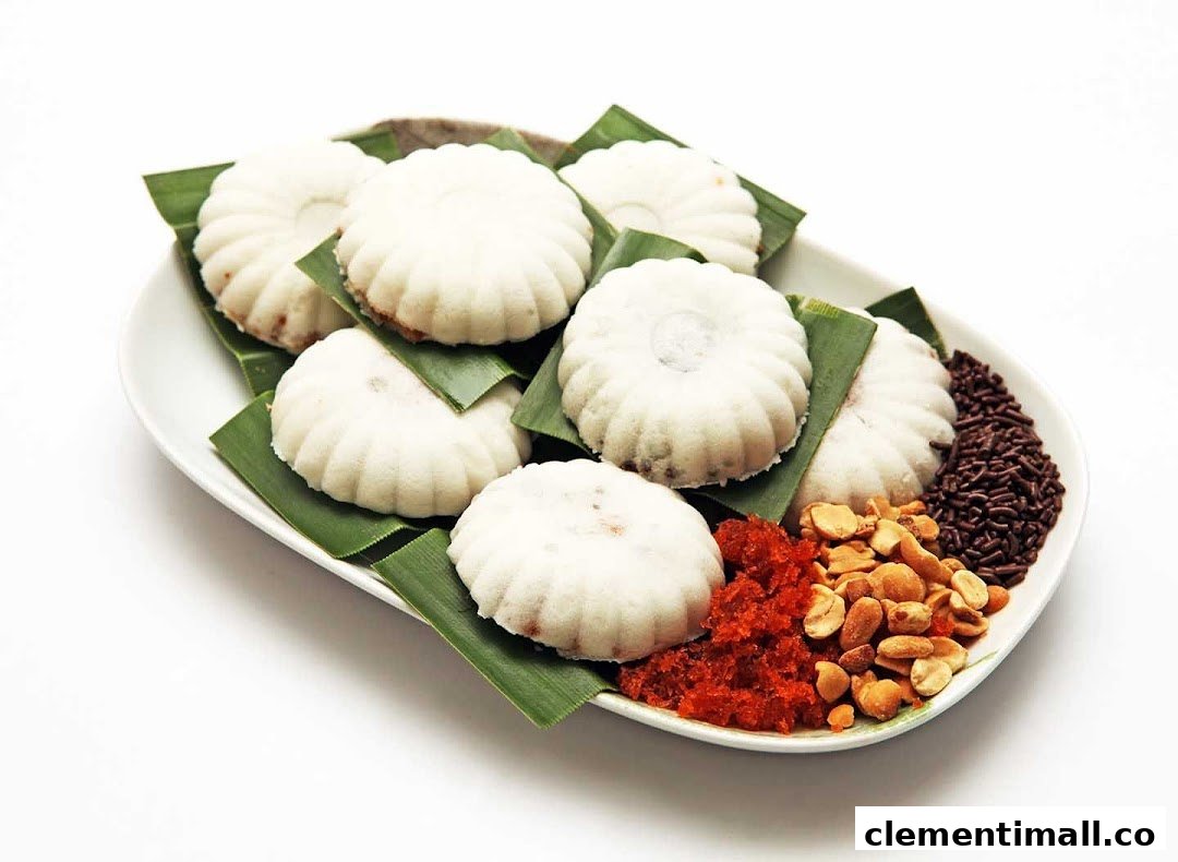 A plate of white, fluted cakes on banana leaves with peanuts, chili, and chocolate sprinkles.