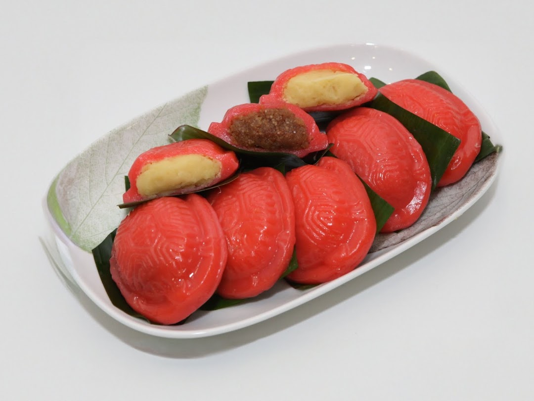 A plate of vibrant red Ang Ku Kueh, some revealing sweet fillings, on a white background.