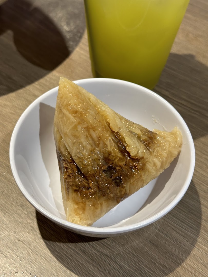 A close-up of a traditional rice dumpling served in a white bowl with a drink in the background.