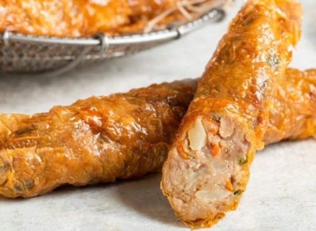 Close-up of two golden-brown fried rolls, one cut open revealing a savory meat and vegetable filling.