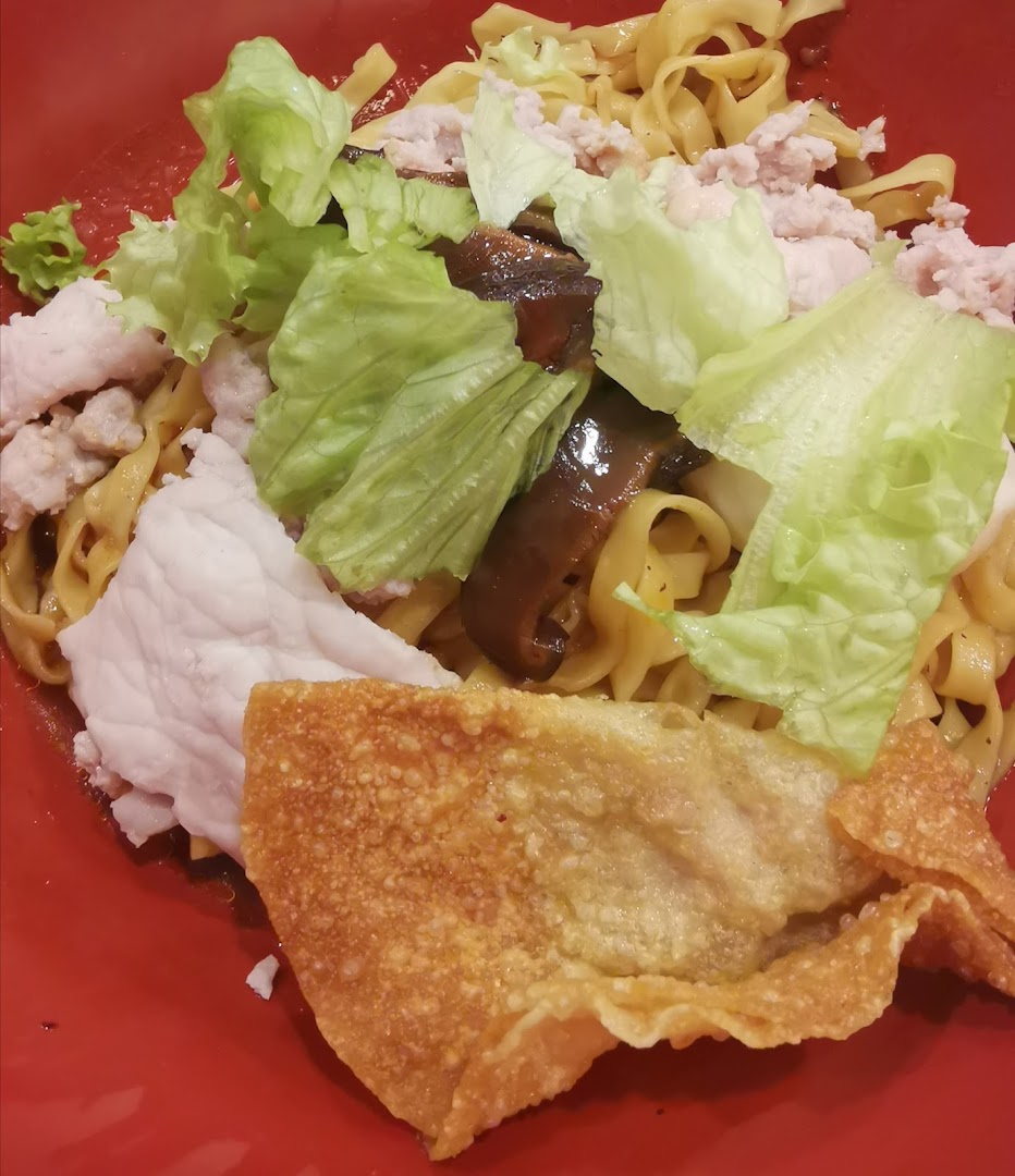 A vibrant red bowl filled with noodles, topped with chicken, lettuce, mushrooms, and crispy wonton.