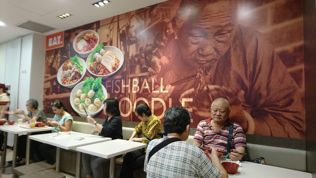 Customers dine inside EAT. restaurant, featuring a large wall mural of fishball noodles and an elderly person.