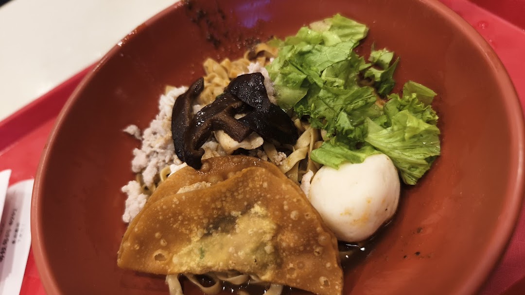 A close-up of a delicious noodle dish with mushrooms, minced meat, fishball, and fried wonton.