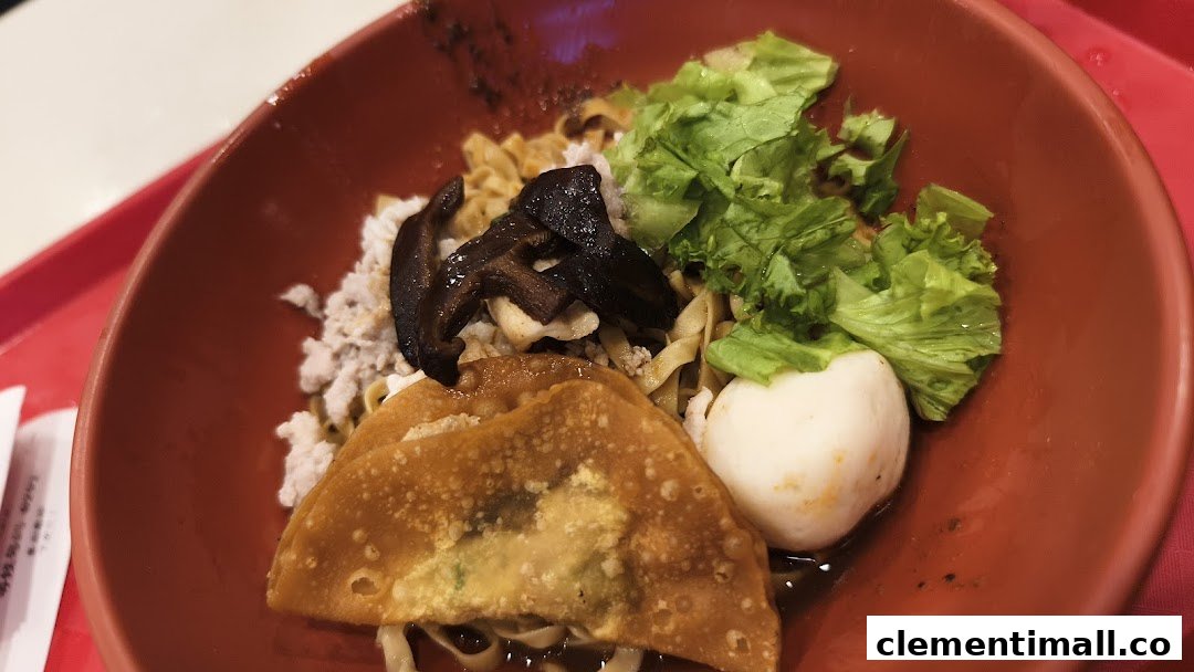 A close-up of a delicious noodle dish with mushrooms, minced meat, fishball, and fried wonton.