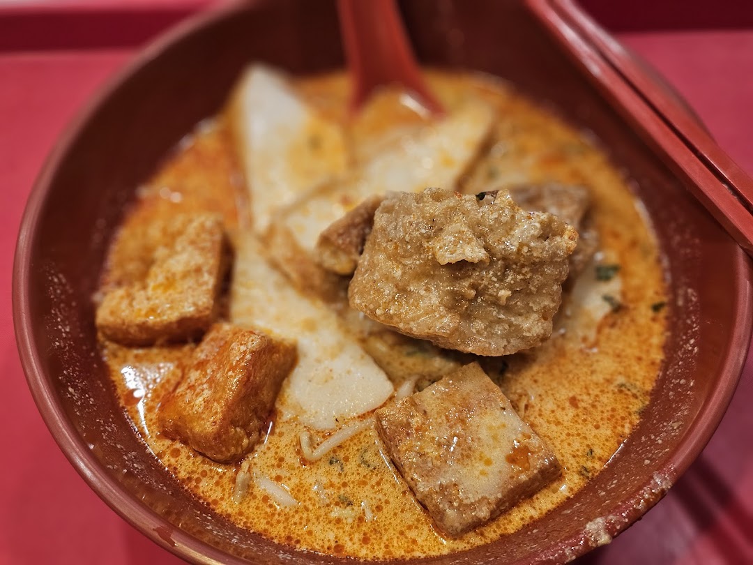 A close-up of a vibrant bowl of curry noodles or laksa with tofu puffs and fish cakes.