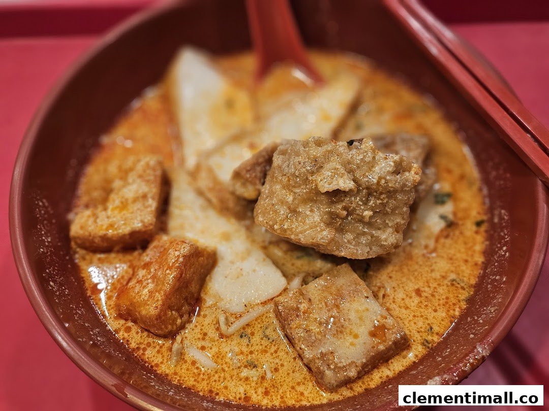 A close-up of a vibrant bowl of curry noodles or laksa with tofu puffs and fish cakes.