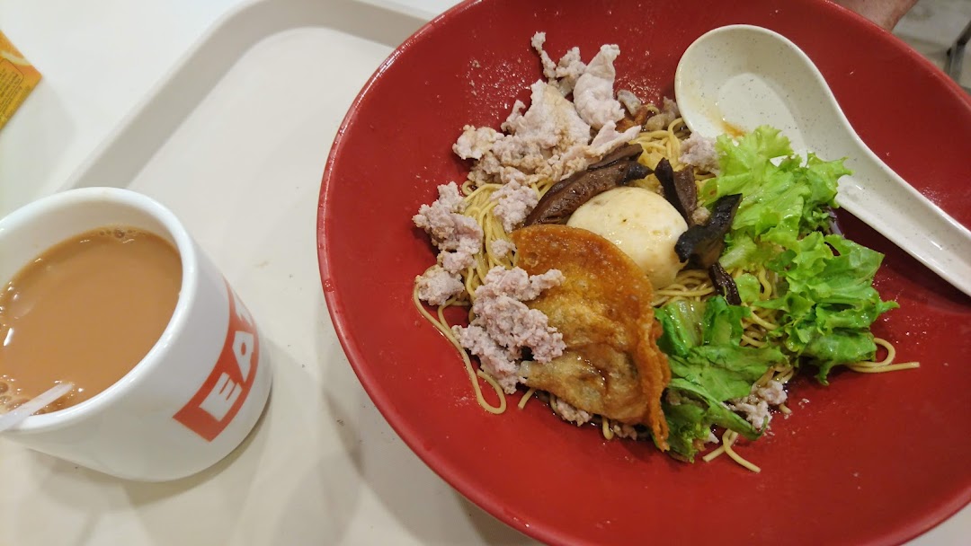 A vibrant red bowl of noodles with various toppings and a cup of milk tea from EAT.