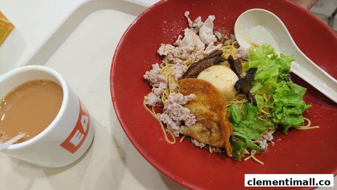A vibrant red bowl of noodles with various toppings and a cup of milk tea from EAT.