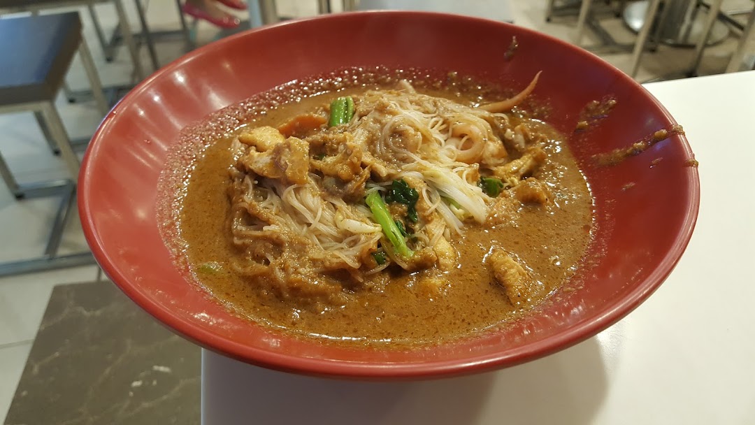 A close-up of a delicious bowl of noodles with a rich, savory sauce and various toppings in a red bowl.