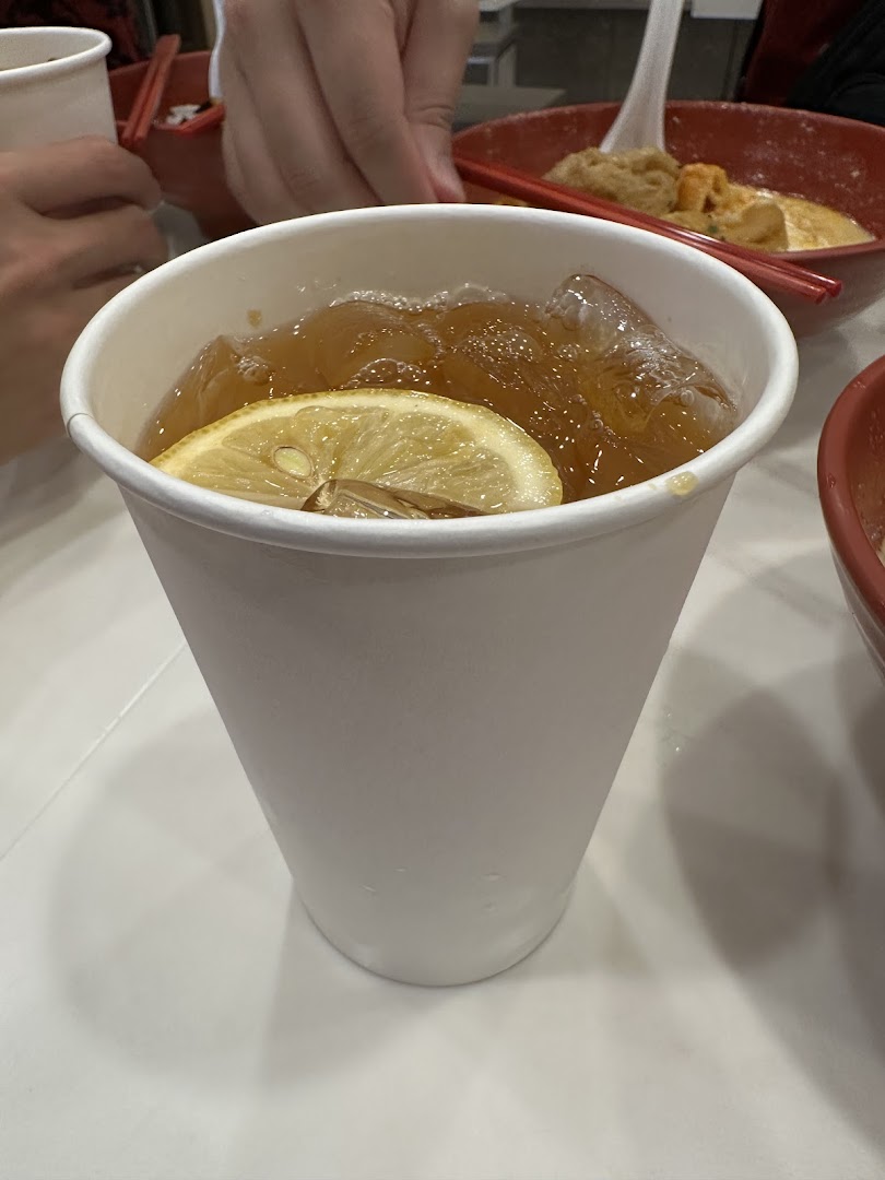 A refreshing iced tea with a lemon slice in a white cup, with food bowls in the background.